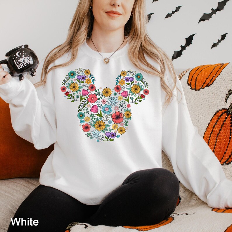 Puede incluir: Sudadera blanca con un dise&ntilde;o floral de Mickey Mouse en varios colores. El dise&ntilde;o est&aacute; centrado en la parte delantera. La palabra "White" est&aacute; impresa en la parte inferior izquierda de la imagen.