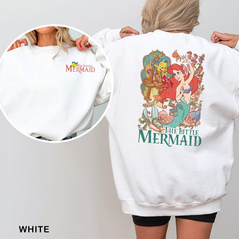 May include: White sweatshirt featuring a colorful graphic of Ariel and Flounder from "The Little Mermaid" on the back. The front left chest has a small embroidered logo. The text "The Little Mermaid" is also displayed.
