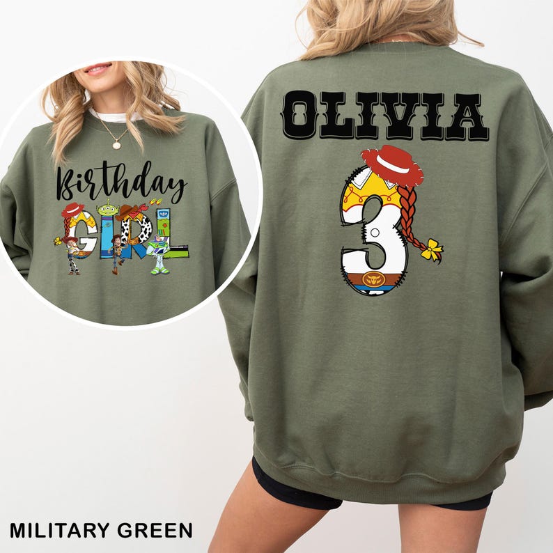 May include: Military green sweatshirt with the text "Birthday GIRL" and character graphics. The back features the name "OLIVIA" and the number "3" with a character design. The sweatshirt is a solid color.