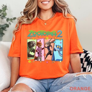 May include: Bright orange t-shirt with the words "ZOOTOPIA 2" above four cartoon character panels. The panels feature a sloth, fox, rabbit, and snake. The word "ORANGE" is printed at the bottom of the shirt.