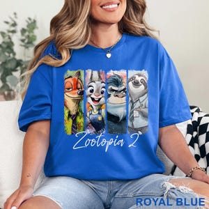 Peut inclure: T-shirt bleu roi avec un motif des personnages de Zootopia 2. Le graphisme comprend Nick Wilde, Judy Hopps et d'autres personnages dans des panneaux verticaux. Les mots "Zootopia 2" sont &eacute;crits en blanc en dessous.