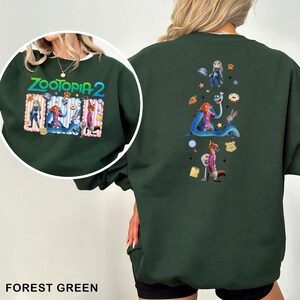 May include: Forest green sweatshirt featuring a colorful graphic of characters from Zootopia 2. The front has a circular design with the movie title and characters. The back has a vertical design with more characters and icons. The sweatshirt is made of a soft material.