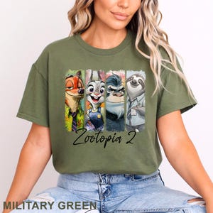 Peut inclure: T-shirt vert militaire avec un imprim&eacute; color&eacute; des personnages de Zootopie. L'illustration comprend Nick Wilde, Judy Hopps, Chef Bogo et Flash. Le texte "Zootopia 2" est &eacute;crit en dessous des personnages.