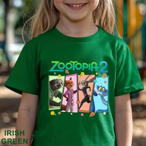May include: A green t-shirt with the words "ZOOTOPIA 2" in teal and white. The shirt features four character panels from the film, including a sloth, fox, rabbit, and snake. The words "IRISH GREEN" are at the bottom.