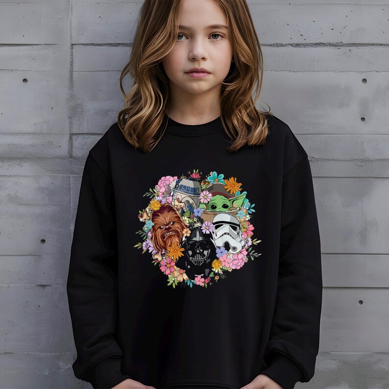 Puede incluir: Sudadera negra con un dise&ntilde;o floral con personajes de Star Wars. El gr&aacute;fico incluye a Chewbacca, Darth Vader, un Stormtrooper, R2-D2 y Grogu, rodeados de flores de colores.