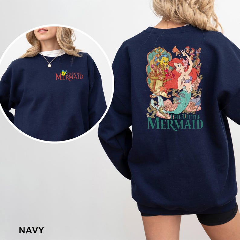 Op de afbeelding: Marineblauw sweatshirt met een kleurrijke afbeelding van Ariel en Botje uit De Kleine Zeemeermin op de rug. De tekst "the little mermaid" in het rood staat op de linkerborst. Het woord "NAVY" staat onderaan de afbeelding.