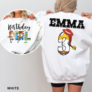 May include: White sweatshirt featuring the text "Birthday Girl" with Toy Story characters. The back of the sweatshirt has the name "EMMA" and the number "3" with a cowgirl design. The sweatshirt is a birthday-themed item.