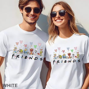 May include: White t-shirts with a cartoon design of characters holding Mickey Mouse-shaped balloons above the word "FRIENDS" in colourful letters. The shirts are worn by two people.