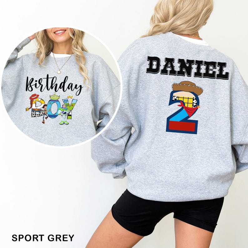 May include: A light gray sweatshirt with the text "Birthday Boy" and cartoon character graphics on the front. The back features the name "DANIEL" above a number 2 with a cowboy hat and bandana design. The sweatshirt is sport grey.
