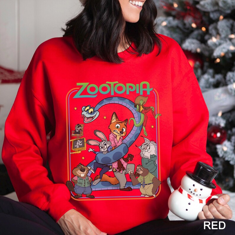 May include: Red sweatshirt featuring a colorful graphic from the movie "Zootopia." The design includes the film's title and various characters like Judy Hopps and Nick Wilde. The sweatshirt is a festive holiday item.