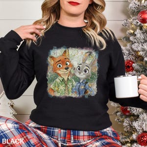 May include: Black crew neck sweatshirt with a colourful graphic of Nick Wilde and Judy Hopps from Zootopia. The image shows the characters in a distressed, vintage style. The word "BLACK" is printed at the bottom of the sweatshirt.