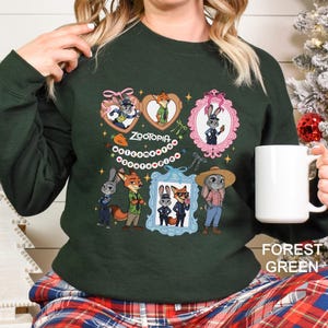 Pode incluir: Camisola verde floresta com personagens de desenhos animados do filme Zootopia. O design inclui imagens emolduradas dos personagens, o t&iacute;tulo do filme e elementos decorativos. Uma caneca branca &eacute; segurada na m&atilde;o.