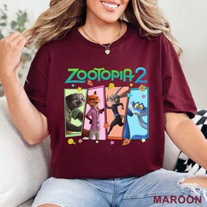 May include: A maroon t-shirt with the text "ZOOTOPIA 2" in green and images of four characters from the film. The characters are in colourful rectangular frames. The word "MAROON" is printed at the bottom of the shirt.
