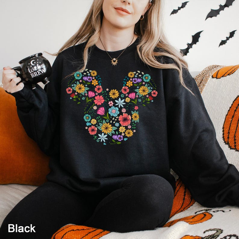 Puede incluir: Sudadera negra con un dise&ntilde;o floral en forma de cabeza de rat&oacute;n. El arreglo floral incluye una variedad de flores coloridas. La palabra "Black" est&aacute; impresa en la parte inferior de la imagen.
