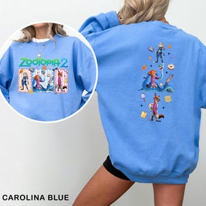 May include: Carolina blue sweatshirt featuring the text "ZOOTOPIA 2" with cartoon characters. The back of the sweatshirt displays additional Zootopia characters. A fun and colorful design for fans of the animated movie.