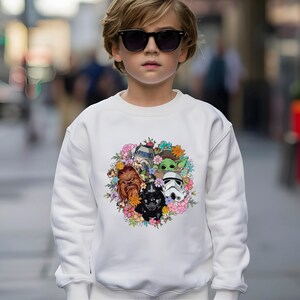 Puede incluir: Sudadera blanca con un dise&ntilde;o de corona floral colorida con personajes de Star Wars. La corona incluye a R2-D2, Grogu, Chewbacca, Darth Vader y un Stormtrooper. La sudadera es de estilo casual y c&oacute;modo.
