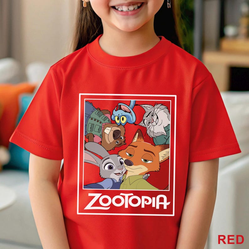 Peut inclure: Un t-shirt rouge avec un graphisme du film "Zootopie". Le motif comprend des personnages comme Judy Hopps et Nick Wilde, encadr&eacute;s dans un rectangle blanc. Le mot "ZOOTOPIA" est imprim&eacute; en blanc en dessous.