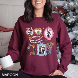 Pode incluir: Camisola bord&ocirc; com personagens de desenhos animados de Zootopia. O design inclui imagens emolduradas de uma raposa e um coelho, com a palavra "Zootopia" e outros elementos decorativos.