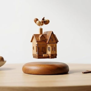 May include: A wooden miniature house with a detailed facade, floating above a wooden base. Brown balloons are attached to the chimney. The house is approximately 4 inches tall.