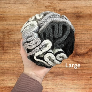 May include: A large, hand-crocheted, gray, black, and white yarn scrunchie. The scrunchie is made with a ruffled design.