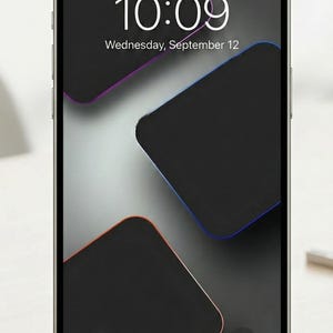 Może przedstawiać: Smartfon wyświetla godzinę 10:09 w środę, 12 września. Ekran ma ciemne tło z trzema czarnymi, zaokrąglonymi prostokątami obrysowanymi na pomarańczowo, niebiesko i fioletowo. Telefon leży na jasnej powierzchni.