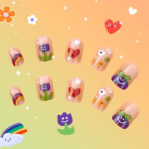 May include: A collection of press-on nails with diverse designs. Some nails display a rainbow, a heart with stars, a smiling flower, and a smiling purple flower. The nails are a nude colour with the designs painted on them.