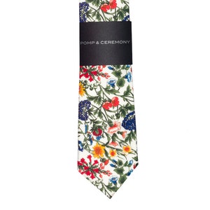 Pode incluir: Gravata floral com fundo branco e padr&atilde;o de flores vermelhas, azuis e amarelas. A gravata tem uma faixa preta com o texto "POMP & CEREMONY". Um acess&oacute;rio cl&aacute;ssico.