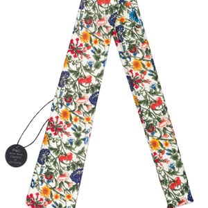 Pode incluir: Gravata com padr&atilde;o floral sobre fundo branco. O design colorido apresenta flores e folhagens vermelhas, amarelas, azuis e verdes. Uma etiqueta preta com texto branco est&aacute; anexada.