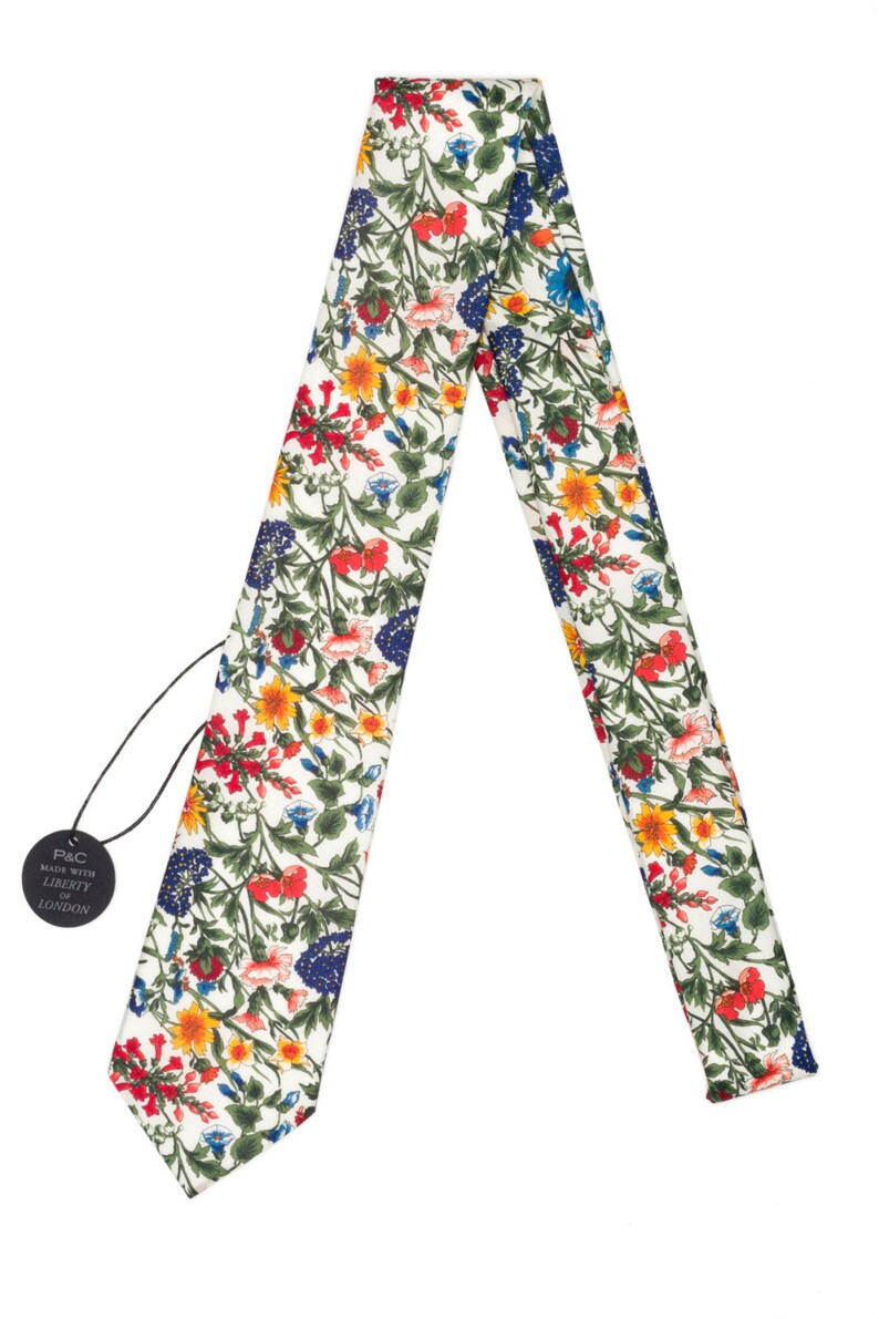 Pode incluir: Gravata com padr&atilde;o floral sobre fundo branco. O design colorido apresenta flores e folhagens vermelhas, amarelas, azuis e verdes. Uma etiqueta preta com texto branco est&aacute; anexada.