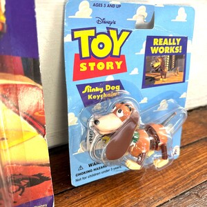 Peut inclure: Un porte-cl&eacute;s Slinky Dog de Toy Story dans son emballage d'origine. L'emballage est bleu avec le logo Toy Story et l'inscription &laquo; REALLY WORKS! &raquo;. Le Slinky Dog est marron et beige. L'emballage indique &laquo; AGES 5 AND UP &raquo;.