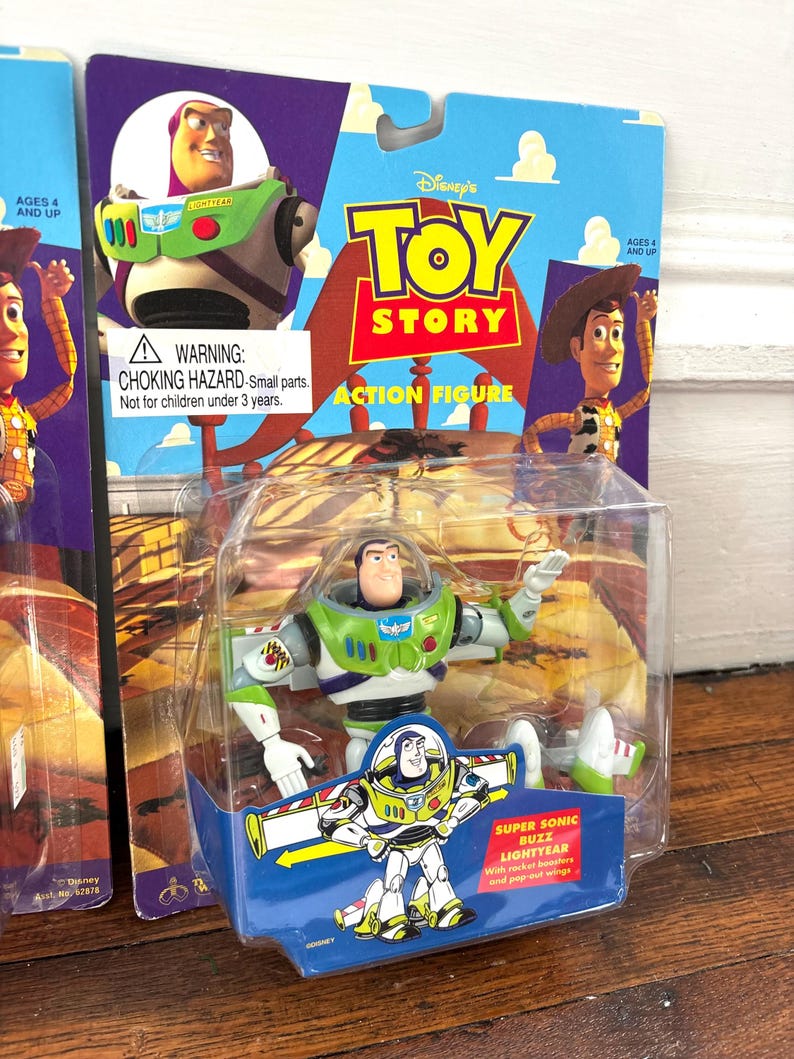 Może przedstawiać: Figurka Buzz Lightyear z filmu Toy Story Disneya, zapakowana na niebiesko-fioletowej karcie. Figurka znajduje się w przezroczystym plastikowym etui. Karta przedstawia Woody'ego i Buzza Lightyeara. Opakowanie zawiera ostrzeżenie o małych częściach.