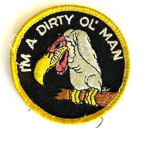 May include: A circular embroidered patch with a black background and a yellow border. It features a white vulture with a yellow beak and red wattle perched on a brown branch. The text "I'M A DIRTY OL' MAN" is embroidered in white.