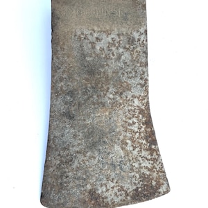 May include: A weathered metal axe head with a rectangular shape and a flared cutting edge. The surface is covered in brown rust and oxidation. The word COLLINS is stamped into the metal near the top edge of the axe head.