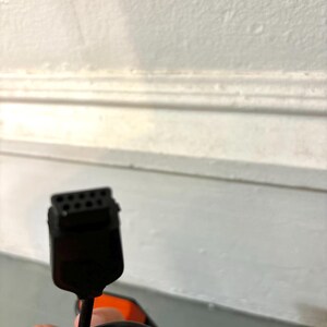 May include: A black electronic connector cable featuring a rectangular head with eight small pin holes arranged in two rows. The cable is black and flexible, extending from the connector head, which has a slightly tapered shape and a smooth finish.