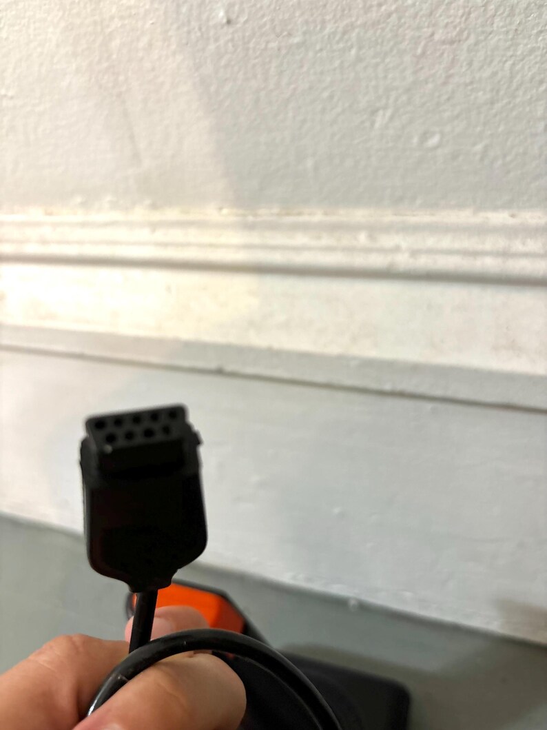 May include: A black electronic connector cable featuring a rectangular head with eight small pin holes arranged in two rows. The cable is black and flexible, extending from the connector head, which has a slightly tapered shape and a smooth finish.