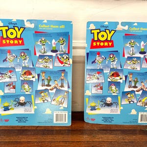 Może przedstawiać: Dwa tyły kart z figurkami Toy Story. Niebieskie karty zawierają zdjęcia Buzza Astrala, Chudego i innych postaci. Logo Toy Story jest w kolorze czerwonym i ż&oacute;łtym. Tekst "Collect them all!" znajduje się na g&oacute;rze.