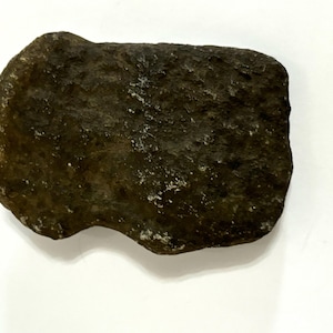 May include: A dark brown, irregularly shaped rock with a rough, textured surface. The rock has a slightly rounded shape with some lighter-colored mineral deposits. The object is set against a white background.