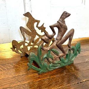 May include: A metal letter holder featuring two stylized figures of greyhounds in a leaping pose. The front figure is painted in a vibrant green, while the rear figure has a rusted, weathered brown finish. Both figures are set against a base.