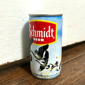 May include: Vintage Schmidt Beer can with a red and yellow logo. The can features a blue background with illustrations of flying ducks. The text "Schmidt BEER" is prominently displayed on the can.