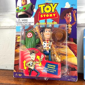 Peut inclure: Figurine Toy Story de Woody dans un emballage plastique. L'emballage pr&eacute;sente le logo Toy Story, Woody et Buzz l'&Eacute;clair. La figurine est &eacute;tiquet&eacute;e "Fighter Woody" et comprend un cactus et un chapeau de cowboy.