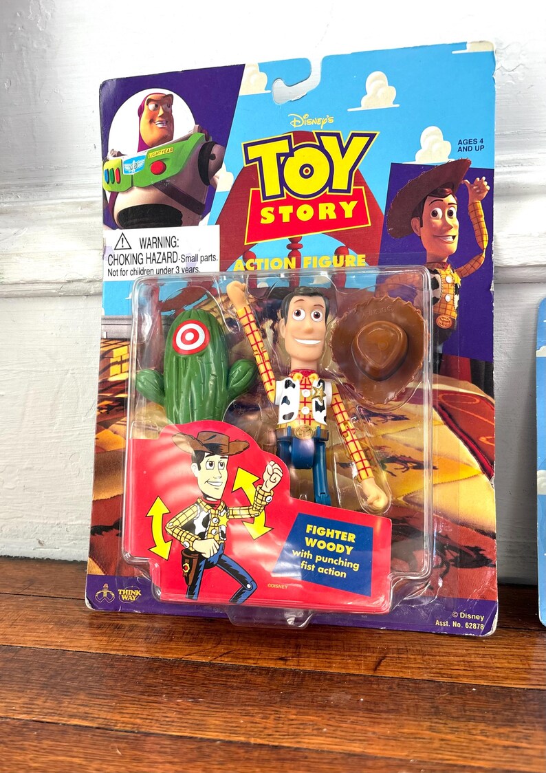 Peut inclure: Figurine Toy Story de Woody dans un emballage plastique. L'emballage pr&eacute;sente le logo Toy Story, Woody et Buzz l'&Eacute;clair. La figurine est &eacute;tiquet&eacute;e "Fighter Woody" et comprend un cactus et un chapeau de cowboy.