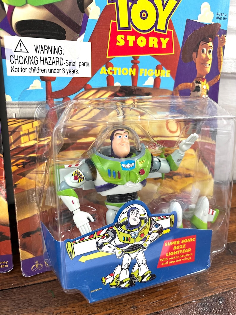 Może przedstawiać: Figurka Buzz Lightyear w oryginalnym opakowaniu. Figurka jest zielona, biała i fioletowa, z przezroczystym plastikowym bąblem. Opakowanie zawiera logo Toy Story i ostrzeżenie o małych częściach.