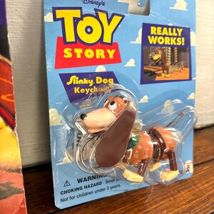 Peut inclure: Un porte-cl&eacute;s Slinky Dog de la franchise Disney Toy Story. L'emballage est bleu avec le logo Toy Story en rouge et jaune. Le porte-cl&eacute;s repr&eacute;sente un jouet Slinky Dog marron et beige. L'emballage indique "Really Works!" et "Ages 5 and Up."
