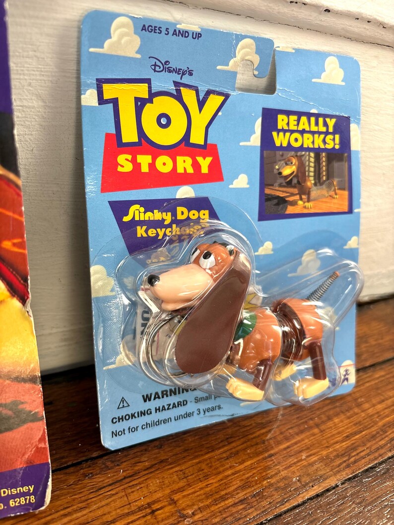 Peut inclure: Un porte-cl&eacute;s Slinky Dog de la franchise Disney Toy Story. L'emballage est bleu avec le logo Toy Story en rouge et jaune. Le porte-cl&eacute;s repr&eacute;sente un jouet Slinky Dog marron et beige. L'emballage indique "Really Works!" et "Ages 5 and Up."