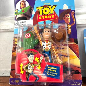 Peut inclure: Figurine articul&eacute;e Woody de Toy Story dans son emballage d'origine. L'emballage pr&eacute;sente des images de Woody, Buzz l'&Eacute;clair et un cactus. La figurine est dans un bo&icirc;tier en plastique transparent, avec l'inscription "Fighter Woody".