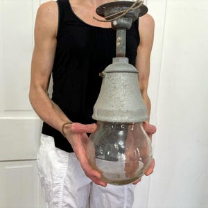 May include: Vintage industrial pendant light with a clear glass bulb enclosure and a galvanized metal shade. The light fixture has a metal top and a cord for hanging. The overall design is rustic and functional.