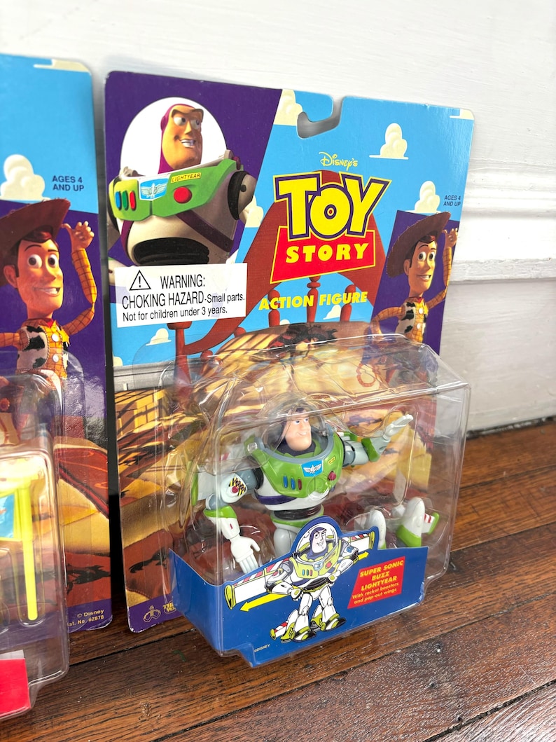 Może przedstawiać: Figurka Buzz Lightyear z Toy Story Disneya, zapakowana w przezroczystą plastikową obudowę. Opakowanie zawiera logo Toy Story, wizerunek Buzza Lightyeara oraz napis "ACTION FIGURE". Figurka jest zielona, biała i fioletowa.