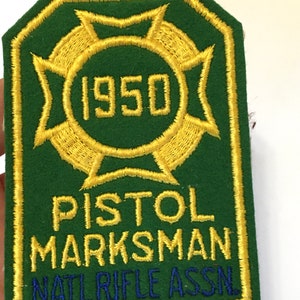 May include: Green felt patch with gold embroidered lettering. The patch reads "Pistol Marksman" and "Natl Rifle Assn." with the year "1950" in a circle.