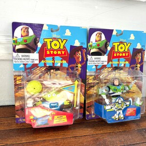 Może przedstawiać: Dwie figurki akcji Toy Story w oryginalnym opakowaniu. Jedna przedstawia Buzza Astrala, druga Obcego. Opakowanie zawiera logo Toy Story, zdjęcia postaci i ostrzeżenie o niebezpieczeństwie uduszenia.