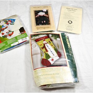 May include: Three Christmas stocking cross-stitch kits. One kit features a snowman with the words "Believe" on the stocking. Another kit features a snowman with a red hat and a blue scarf. The third kit features a Santa Claus with a red hat and a white beard.